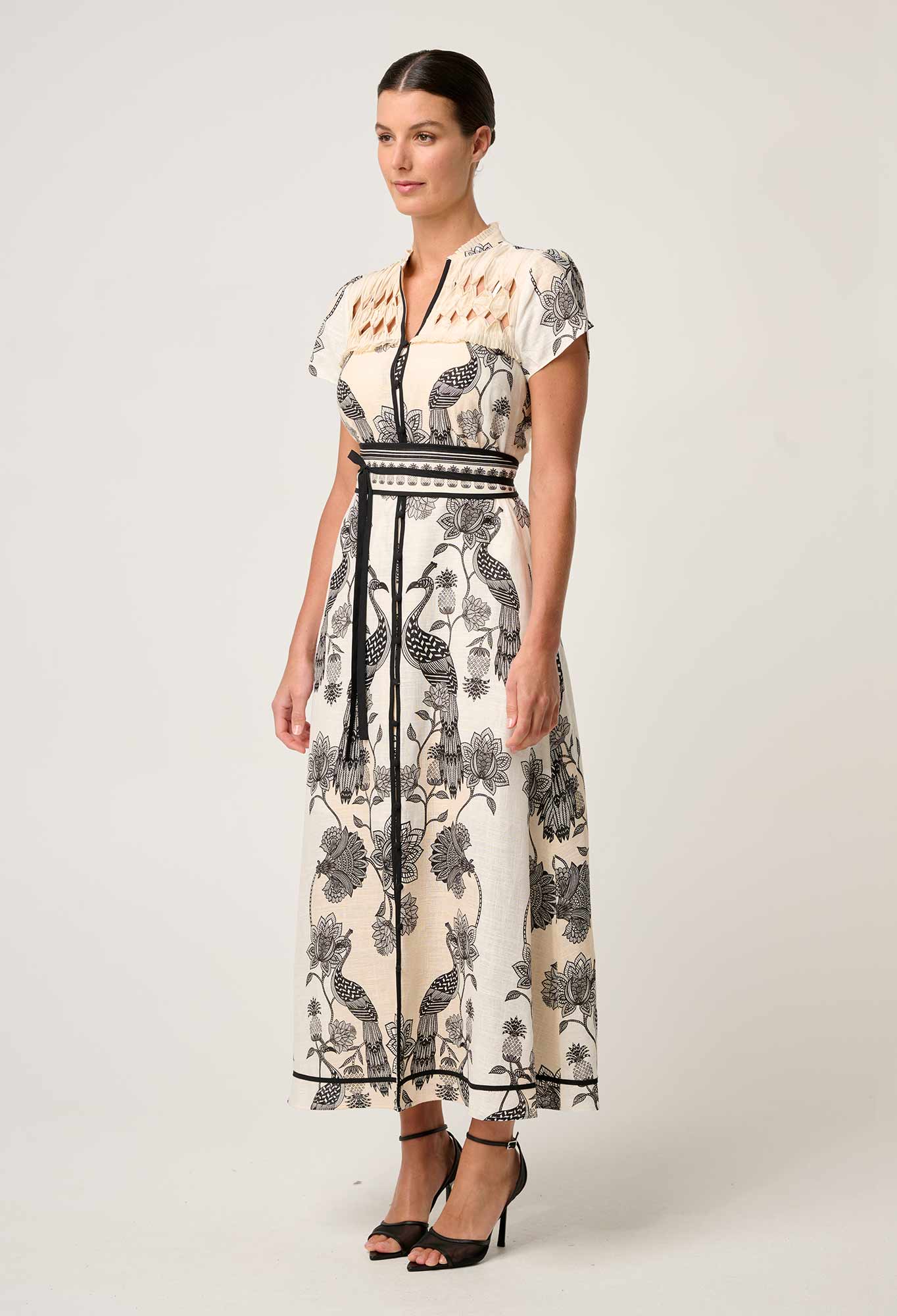 Side angled view of cream and black printed maxi dress with diamond smock yoke and waist belt